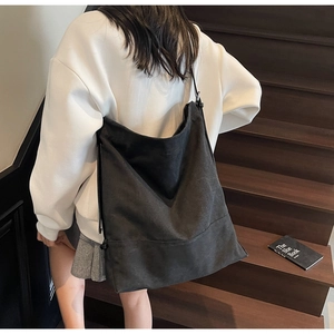Detail of a large capacity black canvas bucket bag carried by a model on stairs