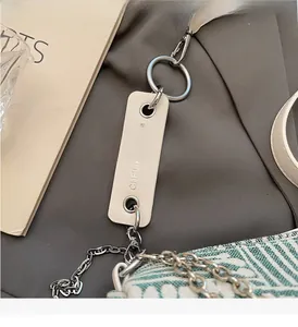 Detail of a chic cream leather tag with a silver chain on a green woven crossbody bag