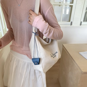 Detail of off-white canvas tote bag featuring blue artistic text and leather pendant
