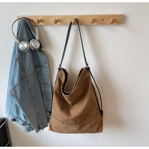 Detail view of a large brown canvas bucket bag hanging with casual lifestyle accessories