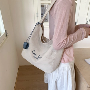 Detail of off-white canvas tote bag featuring blue typography and navy leather pouch