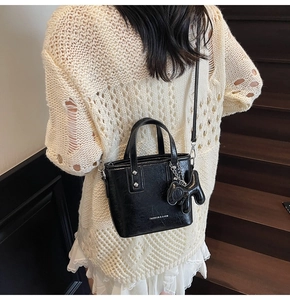 Détail d'un mini tote en cuir noir avec breloque chiot et rivets sur un pull beige