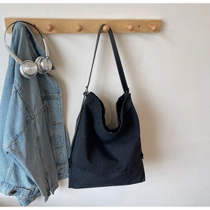 Detail of minimalist black canvas hobo bag hanging on a wall with lifestyle accessories