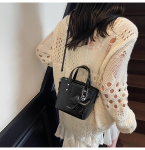Détail du sac seau en cuir noir avec pendentif chien et bandoulière porté par un mannequin