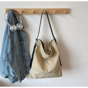 Canvas bucket bag detail with black strap and silver buckle hanging on a wooden rack