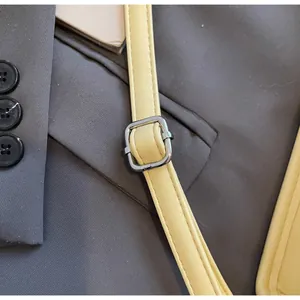 Détail d'une bandoulière en cuir jaune clair réglable avec boucle argentée sur veste grise