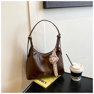 Detail of a brown crescent shoulder bag featuring pebbled texture and a pink plush charm