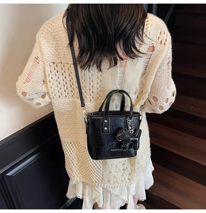 Detail of a black mini tote bag with dog charm and white text, styled on a beige sweater