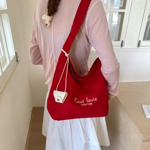 Rear view of model wearing a large red canvas tote bag with white letter embroidery