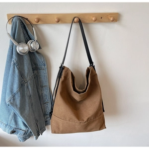 Detail of a brown canvas hobo bag featuring a slim black strap and curved stitching
