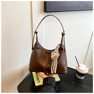 Close-up of dark brown hobo underarm bag with brand logo and cute plush bear charm