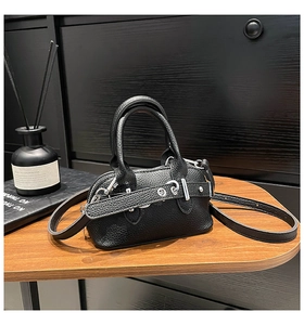 Detail of black pebbled leather mini shell bag with silver hardware on a wooden table