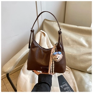 Close-up of a dark brown lychee texture shoulder bag with silver logo and plush charm