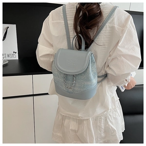 Detail of light blue tweed backpack featuring ENJOY CHANGE embossing and silver metal chain
