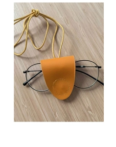 Close-up of a bright yellow leather neck-hanging glasses case on a light wood surface