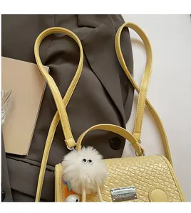 Vue détaillée du sac à dos jaune pâle tressé avec un charmant pompon en peluche blanc