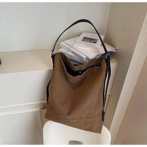 Detail view of large brown canvas bucket bag showing textured fabric and slim shoulder strap