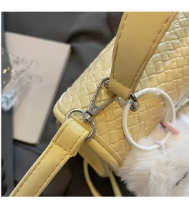 Détail d'un sac en cuir tressé jaune avec fermoir en métal argenté et pompon blanc