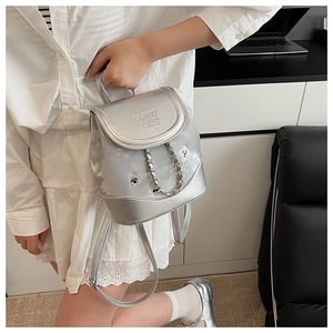 Close-up of a silver metallic mini backpack featuring embossed text and chain detail
