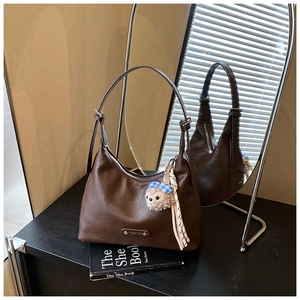 Detail view of a dark brown crescent underarm bag with a cute plush bear charm