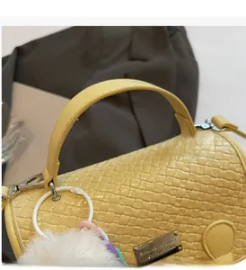 Gros plan du sac à dos jaune en cuir tressé avec boucle métallique et pompon en peluche
