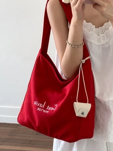 Red canvas tote bag with white embroidery and small beige leather pouch accessory