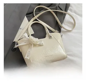 Detail of cream bucket bag showing wrinkled leather texture and elegant pearl bow accents