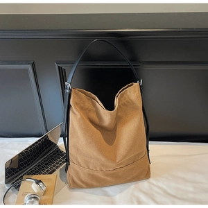 Close-up of a large brown canvas tote bag with slim black straps and wide bottom support