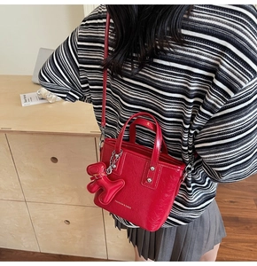 Détail du sac seau en cuir verni rouge avec breloque chien porté par le mannequin