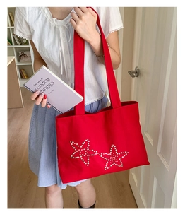 Detail of large red canvas tote bag featuring white pearl star patterns on shoulder strap
