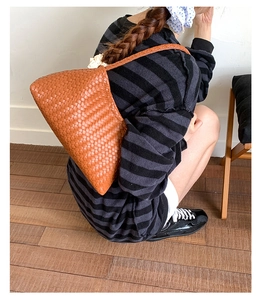 Detail view of brown woven shoulder bag shown with a knit dress in a cozy interior