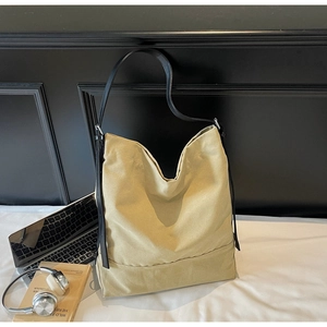 Detail of a large beige canvas tote bag with slim black leather straps for work