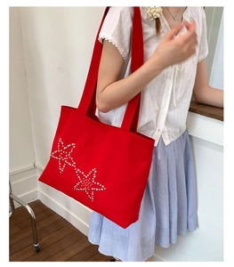 Detail of red canvas tote bag with white star pattern shown on a shoulder model
