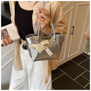 Detail of silver textured tote bag with elegant pearl heart and lace bow accessories