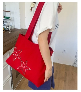 Side view of a red canvas tote bag with sparkling silver rhinestone star details worn by model