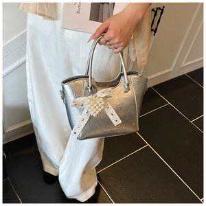 Close-up of metallic silver bucket bag featuring pearl heart charm and bow detail