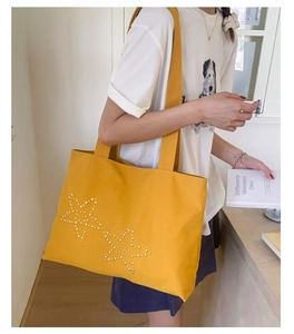 Detail view of yellow canvas tote bag with decorative metallic star studs on the front