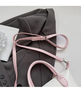 Détail d'un sac seau blanc minimaliste avec bandoulière en cuir rose et boucles argentées