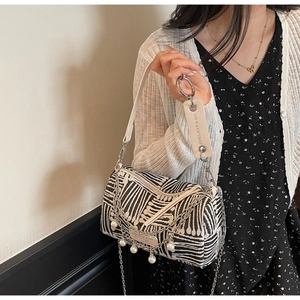 Detail of striped canvas barrel bag with elegant pearl charms and silver metal chain