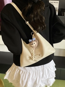 Chic cream hobo shoulder bag with plush bear charm worn by a model in casual style