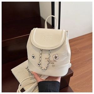 Close-up of cream mini backpack with metal chain and cute bear embroidery on wood stairs
