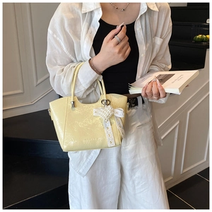 Detail of yellow bucket bag featuring a pearl heart charm and delicate lace bow accent