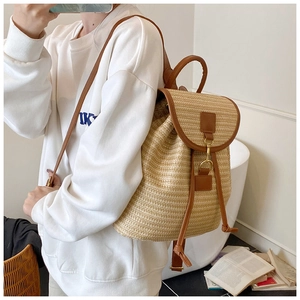 Detail of woven straw backpack with brown leather trim shown on model for realistic size