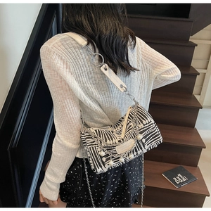 On-shoulder view of black and white woven canvas bag with pearl charm and chain