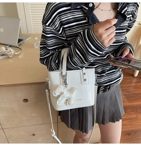 Détail du sac seau en cuir blanc avec pendentif chiot pelucheux et bandoulière réglable