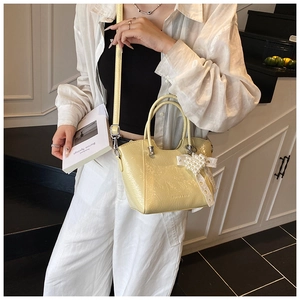 Detail of light yellow bucket bag with pearl heart pendant and lace bow on a model