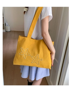 Side view of yellow canvas tote bag with pearl star patterns shown on model shoulder
