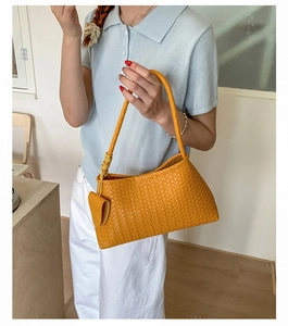 Detail of yellow woven leather texture on a minimalist shoulder bag with hanging charm