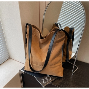 Detail of dark brown canvas bucket bag with leather strap on a wooden surface