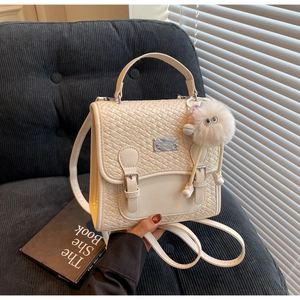 Détail du sac à dos tressé crème avec boucles argentées et un porte-clé en peluche blanc